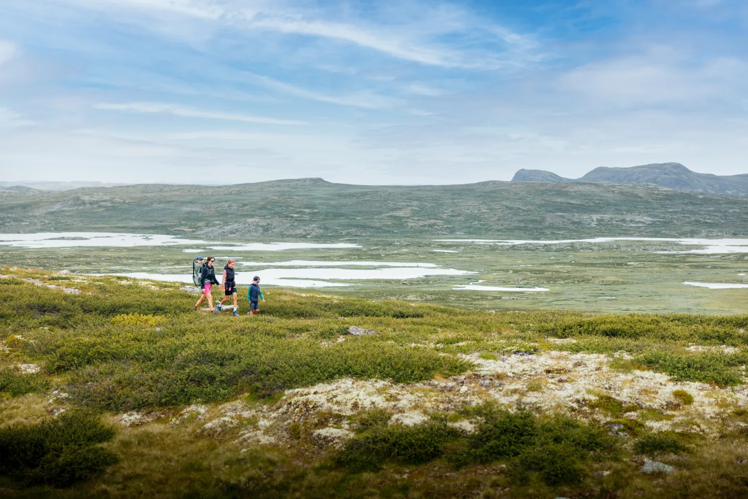 Familie på fjelltur mot Tuva Turisthytte med fjell i bakgrunnen på sommeren